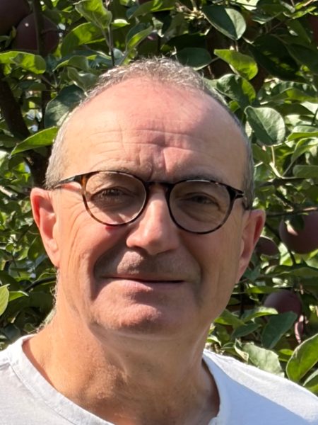 Gord Lovegrove in round glasses and a white t-shirt, in front of a fruit tree