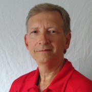 Brian Rogers smiling in a red polo shirt against a white backdrop