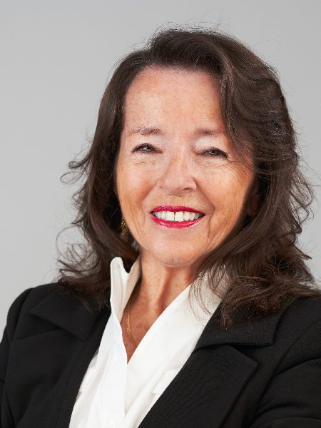 Susan Ames smiling in a black blazer and white blouse against a grey background