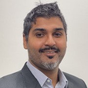 Bal Grewal smiling in a grey blazer and collared shirt against a white background