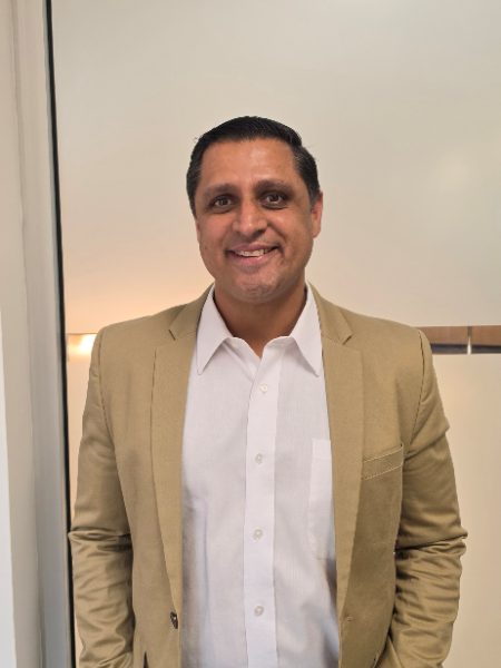 Indy Dhial smiling in a tan blazer and white shirt