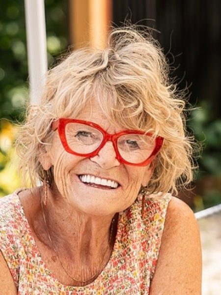 Deb Dickerson-Pogue laughing in red glasses and a flowered top, outdoors