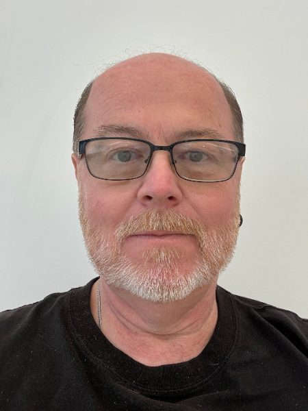 Randy Millis in glasses and a black t-shirt against a white wall