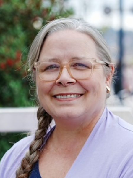 Crystal Dougan smiling outdoors in glasses and a lilac top, with her hair in a braid