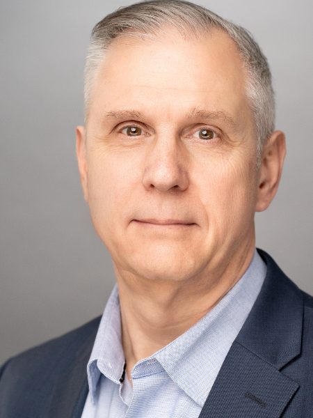 Tim Down in a navy blazer and light blue shirt against a grey background