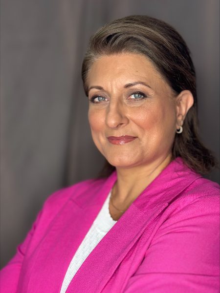 Doris Maria Bregolisse smiling in a bright pink blazer against a grey curtain